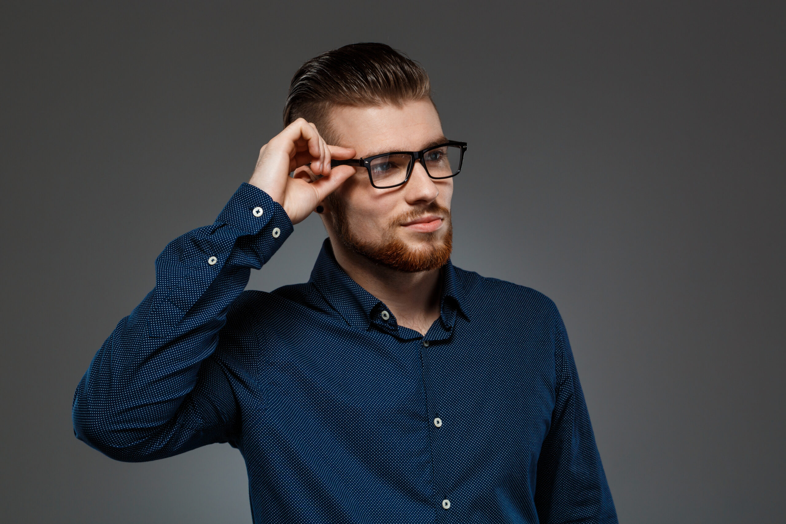 Young successful businessman in glasses posing over dark background. Copy space.